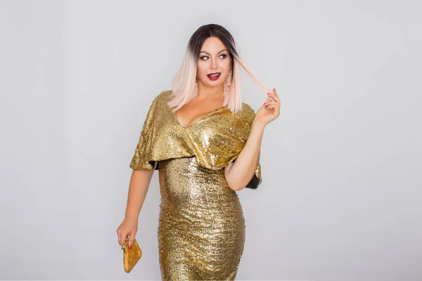 Charming young blonde haired woman wearing elegant gold evening dress and holding gold color clutch in her hands — Stock Photo, Image