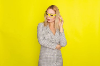 Sarı arka planda, ekose ceketli çekici sarışın kadın. Sarı gözlüklü.