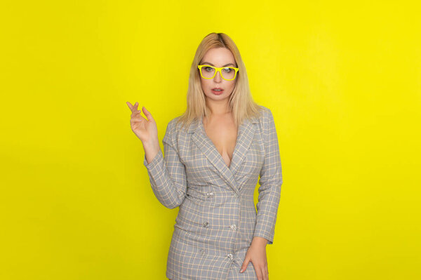 Attractive blonde woman in plaid jacket dress over yellow background wearing yellow glasses