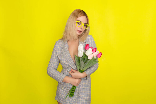 Blonde woman in plaid dress holding tulips bouquet over yellow background