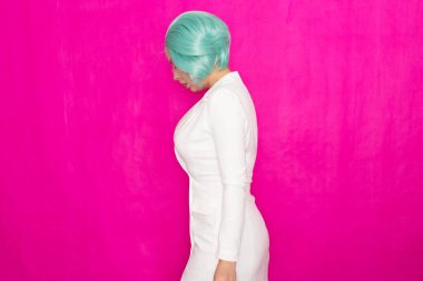 Mentollü kısa saçlı, beyaz bir iş elbisesi içinde stüdyoda fuşya arka planında poz veren güzel bir genç kadın.