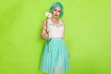 Stüdyo portresi, beyaz bluzlu, açık mavi etekli, yeşil arka planda büyük bir papatya çayı tutan güzel, nane rengi saçlı bir kadın.