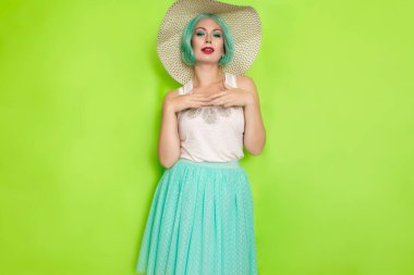 Beyaz bluzlu, mavi etekli, siyah ve beyaz şapkalı güzel, genç, nane rengi saçlı bir kadın. Stüdyo fotoğrafı yeşil arkaplan üzerinde