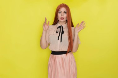 Pembe bluzlu ve etekli, sarı arka planda poz veren genç, güzel, kızıl saçlı bir kadın. Yaz konsepti