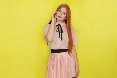 Pembe bluzlu ve etekli, sarı arka planda poz veren genç, güzel, kızıl saçlı bir kadın. Yaz konsepti