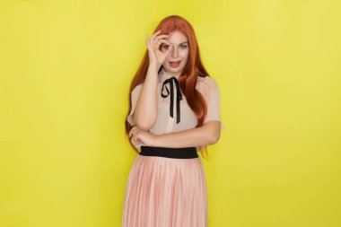 Pembe bluzlu ve etekli, sarı arka planda poz veren genç, güzel, kızıl saçlı bir kadın. Yaz konsepti