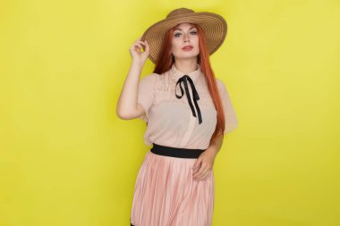 Sarı arka plan, stüdyo, tarz, yaz konsepti üzerinde hasır şapkalı kızıl saçlı kadın.