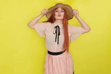 Sarı arka plan, stüdyo, tarz, yaz konsepti üzerinde hasır şapkalı kızıl saçlı kadın.