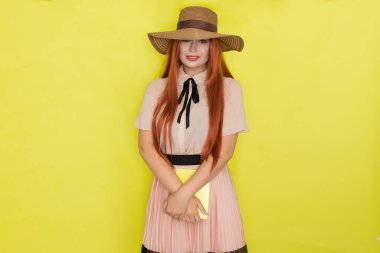 Sarı arka planda saman şapkalı kızıl saçlı kadın elinde kitap tutuyor, stüdyo, tarz, yaz konsepti.