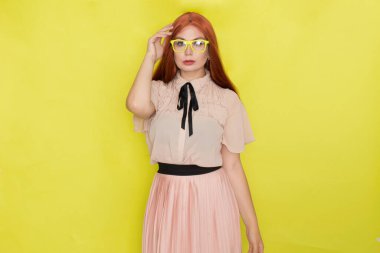 Sarı arka plan, stüdyo, tarz, gözlüklü ve ofis elbiseli kızıl saçlı kadın.
