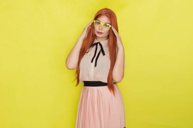 Sarı arka plan, stüdyo, tarz, gözlüklü ve ofis elbiseli kızıl saçlı kadın.