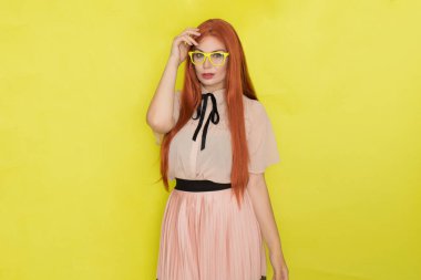 Sarı arka plan, stüdyo, tarz, gözlüklü ve ofis elbiseli kızıl saçlı kadın.
