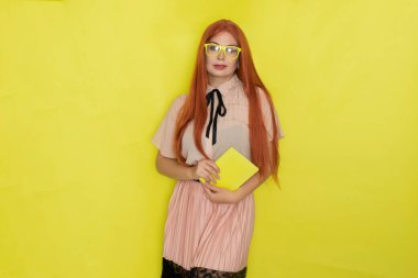 Sarı arka plandaki kızıl saçlı kadın elinde kitap tutuyordu, stüdyo fotoğrafı, poz veriyordu.