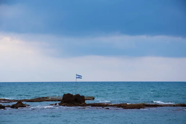 Bandera de Israel en las rocas en el mar cerca de la costa de Tel Aviv. Historia israelí, cultura, política, celebración del Día de la Independencia, conceptos de identidad. Fondo patriótico . — Foto de Stock
