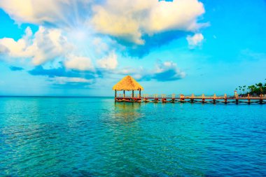 Tropikal beyaz kumlu plaj. Palmiye yaprağı çatılı ahşap iskele sahilde gazebo ile. La Romana, Dominik Cumhuriyeti. 