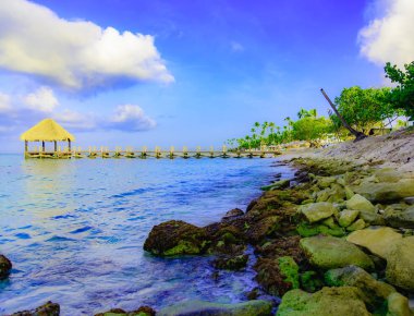 Tropikal beyaz kumlu plaj. Palmiye yaprağı çatılı ahşap iskele sahilde gazebo ile. La Romana, Dominik Cumhuriyeti. 