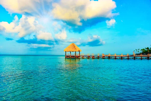 Tropikal beyaz kumlu plaj. Palmiye yaprağı çatılı ahşap iskele sahilde gazebo ile. La Romana, Dominik Cumhuriyeti. 
