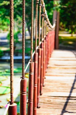 Dar askıya alınmış ahşap köprü üzerinde bir ip su üstünde asılı. Yeşil bitki örtüsü ile Vietnam tropikal park