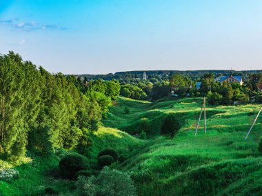 Yeşil çimenler ve ağaçlarla kaplanmış kırsal alan geçidi. Arka planda Hıristiyan kilisesinin çan kulesi