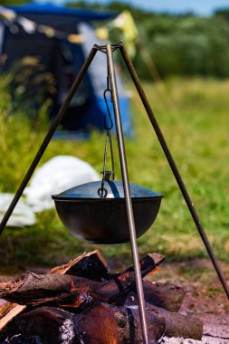 Kamp tenceresi, bir turist kampındaki üç ayaklı bir kampta kamp ateşinin üzerinde asılı duruyor.