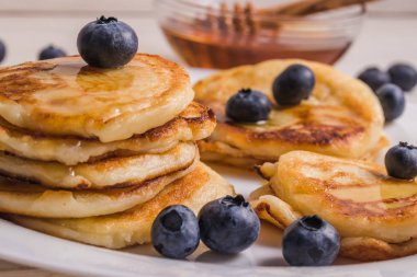 Yaban mersini ile bir tabak üzerinde Cheesecakes, arka planda bal ve bal için tahta bir kaşık ile bir tabak.