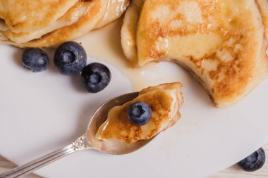 Beyaz bir tabak üzerinde cheesecake bal ve yaban mersini parçaları ile Kaşık.