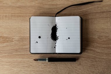 Dolma kalem üstünde bir defter. Siyah mürekkep sıçrama. Ahşap masa. Kopya alanı.