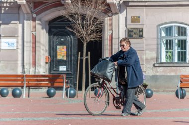 Sokakta yürüyen kadın onun bisiklet ile bir çanta taşıyor. Gerçek insanlar. Arkadan görüntülemek.