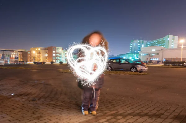Mother and son drawing a heart with sparkle sticks. Light painting. Long exposure