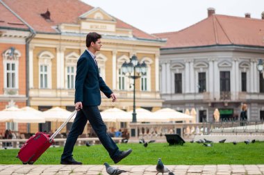 Timisoara, Romanya - 09 Nisan 2016: Sokaklarda yürüyen adam. Takım elbiseli bir adam bavulunu taşıyor. Gerçek insanlar..