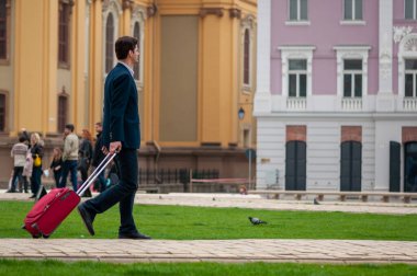 Timisoara, Romanya - 09 Nisan 2016: Sokaklarda yürüyen adam. Takım elbiseli bir adam bavulunu taşıyor. Gerçek insanlar..