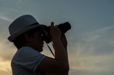 Kameralı çocuk gökyüzünde uçak arıyor.