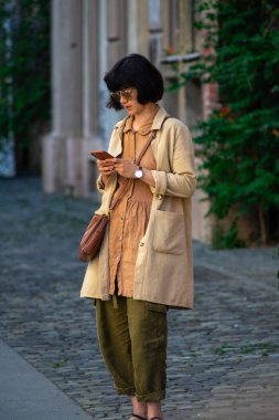 Timisoara, Romanya - 05 Eylül 2020: Sokakta oturan ve telefonunu kontrol eden kadın. Gerçek insanlar..