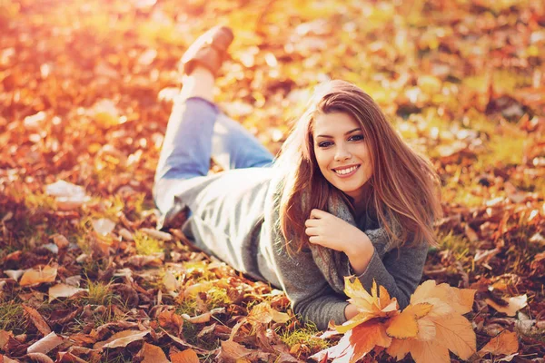 Yaprakları park içinde Güneşli sonbahar gününde yatan genç kadın. Doğal ışık, filtre uygulanan.