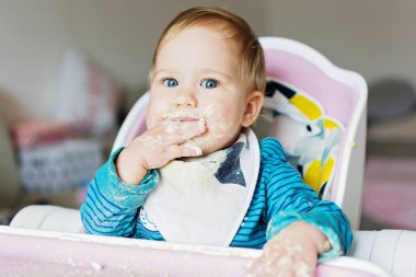 Dağınık yüzlü ve elleriyle kendini besleyen sevimli bir bebek. Sevimli bebek tek başına yemek yiyerek yemeği berbat ediyor. Sütten kesilme..