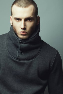 Erkek güzellik kavramı. Yüksek yakalı kazak giyen ve gri arka plan üzerinde poz kısa saçlı acımasız genç adam portresi. Modern sokak stili. Yakın çekim. Stüdyo vurdu