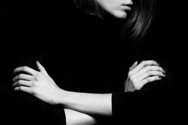 #metoo movement concept. Closeup portrait of young woman hiding face, posing with crossed hands, isolated on black background. Human emotion, expression, rights & communication. Text space. Monochrome studio shot clipart