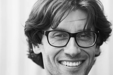 Gözlük kavramı. Işık gri arka plan üzerinde ayakta olgun adam portresi. Uzun dalgalı saçlar. Yakın çekim. Beyaz parlak bir gülümseme. Boşluk. Açık tek renkli vurdu