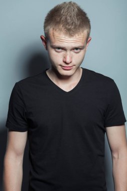 Kısa sarı saçları ve siyah t-shirt giyen ve gri arka plan üzerinde poz yüzündeki çiller ile komik gülümseyen genç adam portresi. Hippi tarzı. Stüdyo vurdu