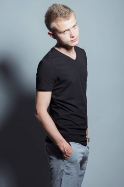 Komik kısa sarı saçlı Genç adam gülümseyen portresi çilli siyah t-shirt giyen ve elleri ceplerinde gri arka plan üzerinde poz yüzünde. Hippi tarzı. Stüdyo vurdu