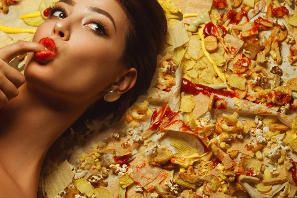 不健康な食事 後党概念 横になっている チップ ポップ コーン ケチャップ ポテト フライを楽しんでいる流行の若い女性の肖像画 完璧な肌 — ストック写真