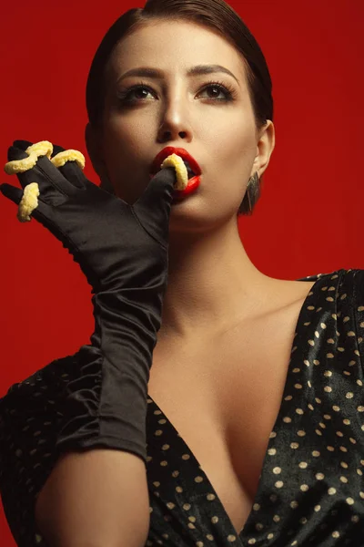 不健康な食事 ジャンク フードの概念 食べて 身に着けているファッショナブルな若い女性の肖像画は揚げ彼女の指および赤い背景にポーズに魚の目です クローズ アップ スタジオ撮影 — ストック写真