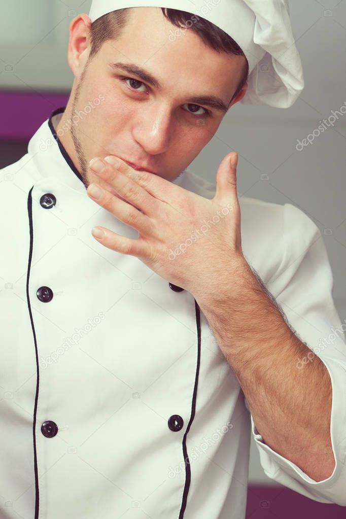 Cooking process concept. Portrait of working young cute man in cook uniform making food in modern kitchen and tasting result. Close up. Indoor shot