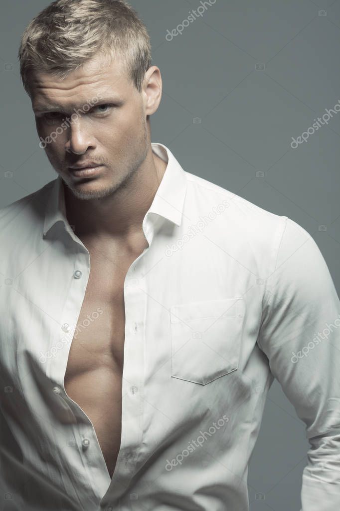 Male fashion, beauty concept. Portrait of brutal young man with short wet blond hair wearing white shirt, posing over gray background. Classic style. Studio shot