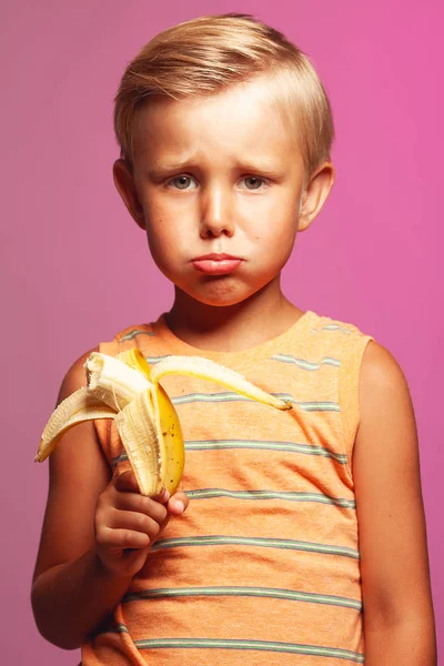 Besviken stiliga barn med blont hår håller banan — Stockfoto