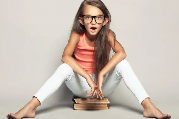 Портрет шокированной смешной девушки, сидящей на книгах — стоковое фото