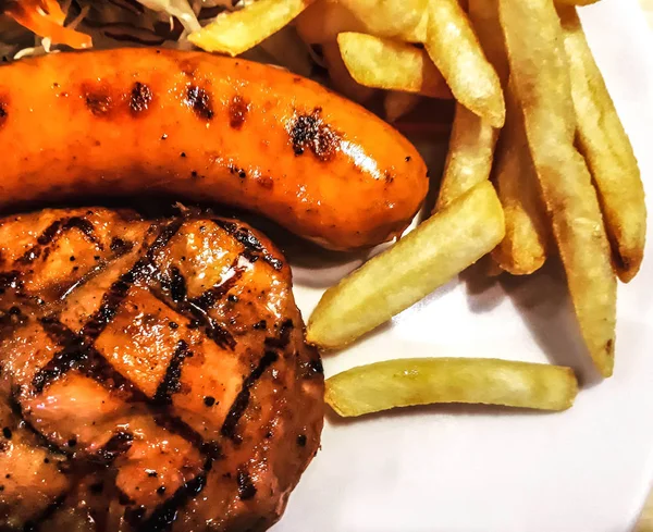 Domuz biftek yakın yukarı beyaz tabak üzerinde ızgara sosis, beyaz çanak üzerinde barbekü biftek ve sosis yakın