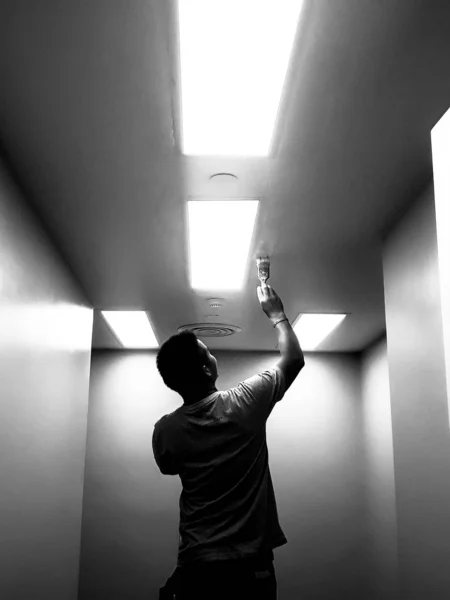 The black silhouette of the technician working on the ceiling, Workers are painting bright ceilings on large ceilings, Silhouette technician who painted the ceiling painted with fluorescent lighting