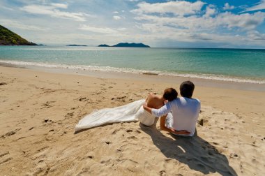 Gelin ve damat düğün elbiseli okyanusun üzerinde oturan ve uzaktan izliyor. Arkadan görüntülemek.