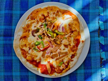 Pastırma ve yeşil baharatlı biber bir plaka üzerinde mavi bir masa örtüsü üzerinde pizza. Üstten görünüm.